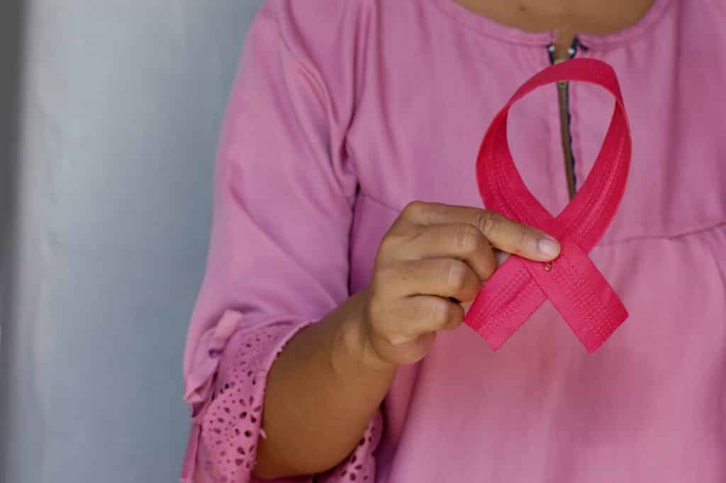 Mulher segurando um laço em homenagem ao Outubro Rosa.