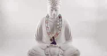 Imagem da estátua de Buddha em posição de meditação. No pescoço dele, uma japamala colorida feita de miçangas.