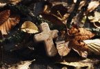 Imagem de um chão repleto de folhas secas e sobre elas uma pequena cruz, simbolizando um retiro espiritual.