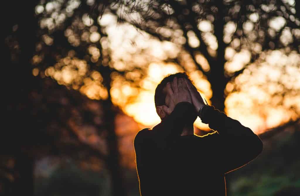 Homem estressado com as mãos sobre o rosto, em um parque, ao pôr do sol.