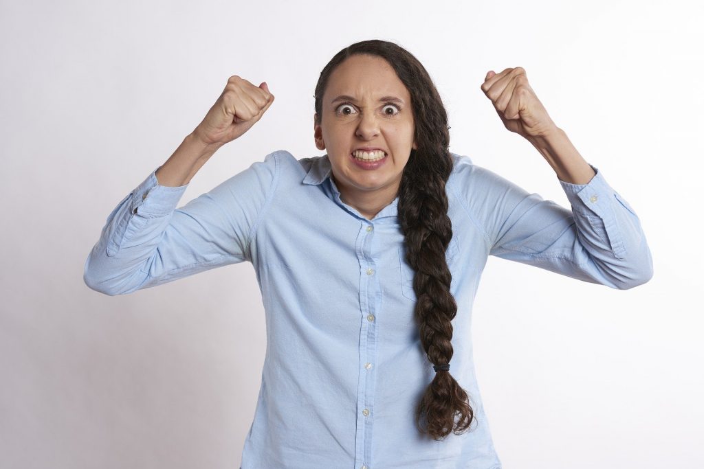 Imagem de uma mulher de mau humor. Ela usa uma camisa azul clara e uma trança longa em seu cabelo.