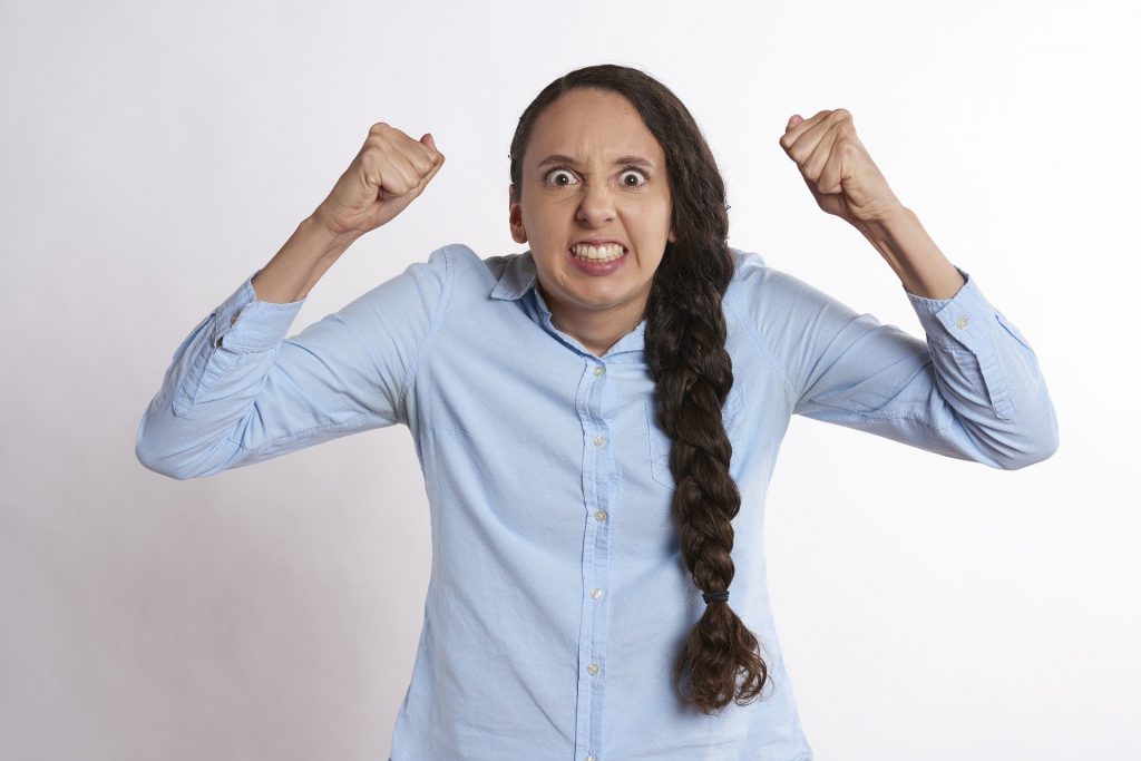 Imagem de uma mulher de mau humor. Ela usa uma camisa azul clara e uma trança longa em seu cabelo.
