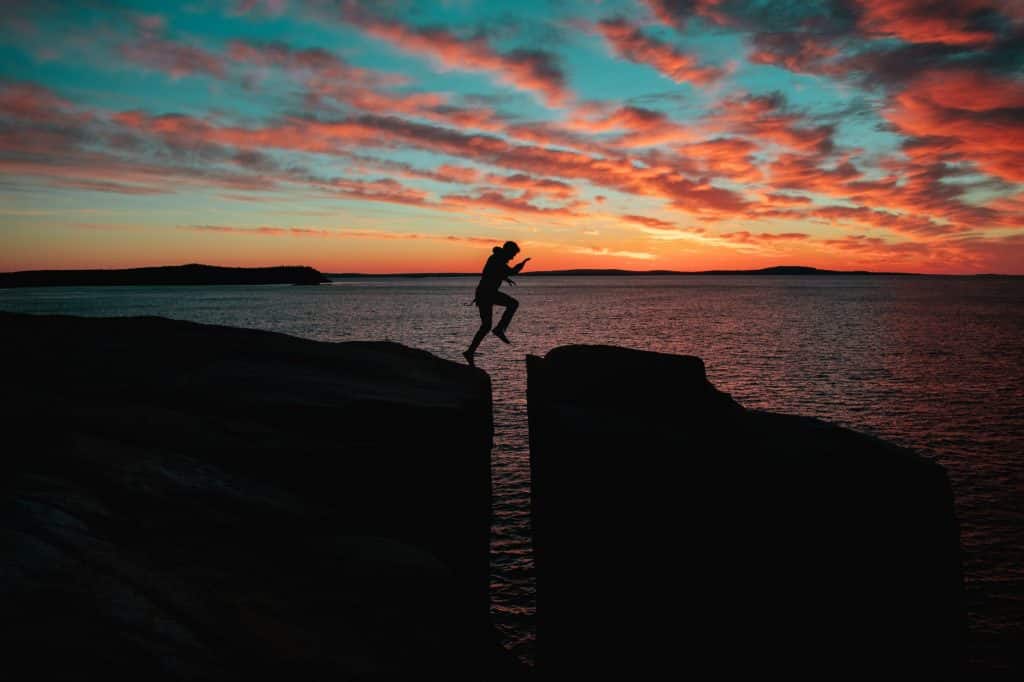 Homem pulando entre pedras durante o pôr-do-sol.