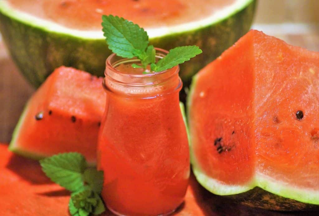 Imagem de vitamina de melancia com iogurte natural disposta em um jarro de vidro decorado com hortelã.