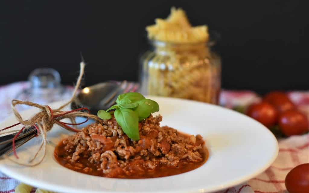 Prato servido com molho de carne moída com talheres apoiados ao lado, decorado com folhas verdes.