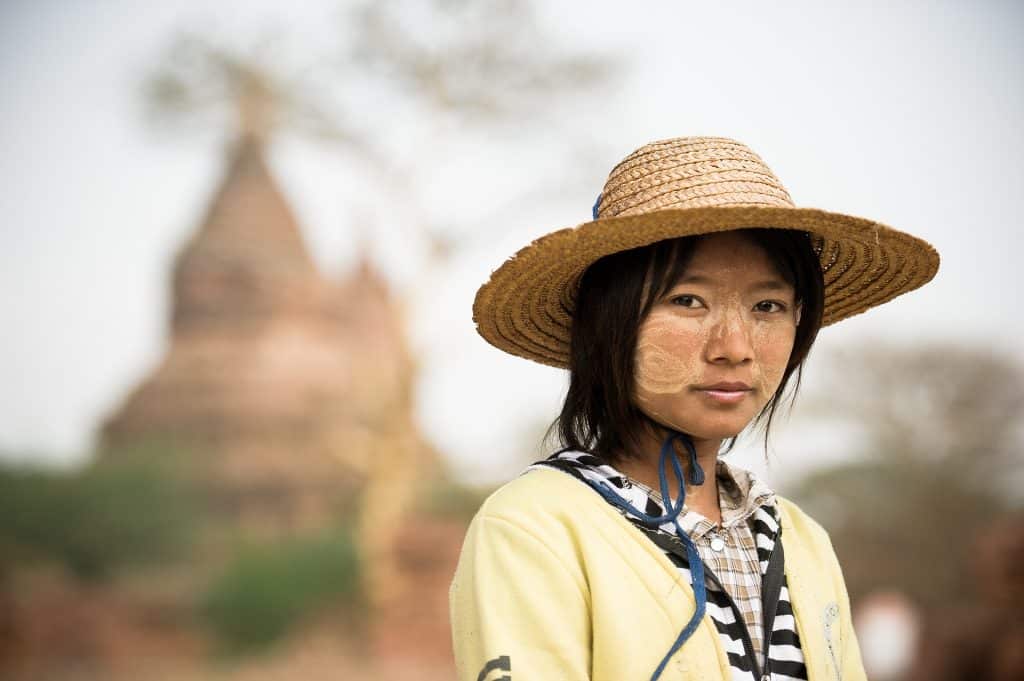 Imagem de uma linda jovem oriental. Ela usa sobre a sua cabeça um chapéu de palha para se proteger do sol.