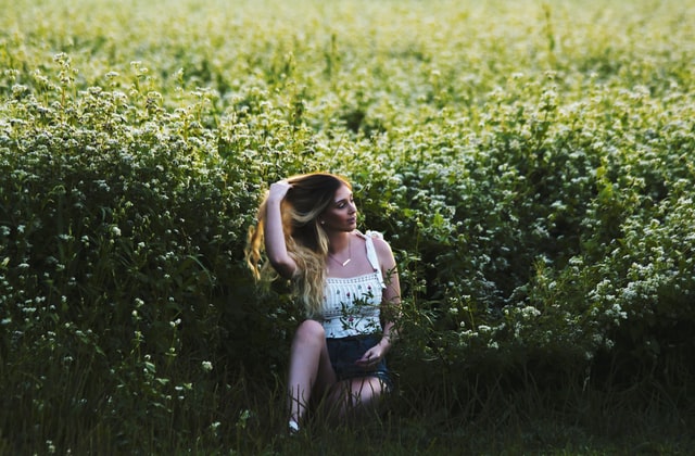 Mulher branca loira no meio de campo de flores.