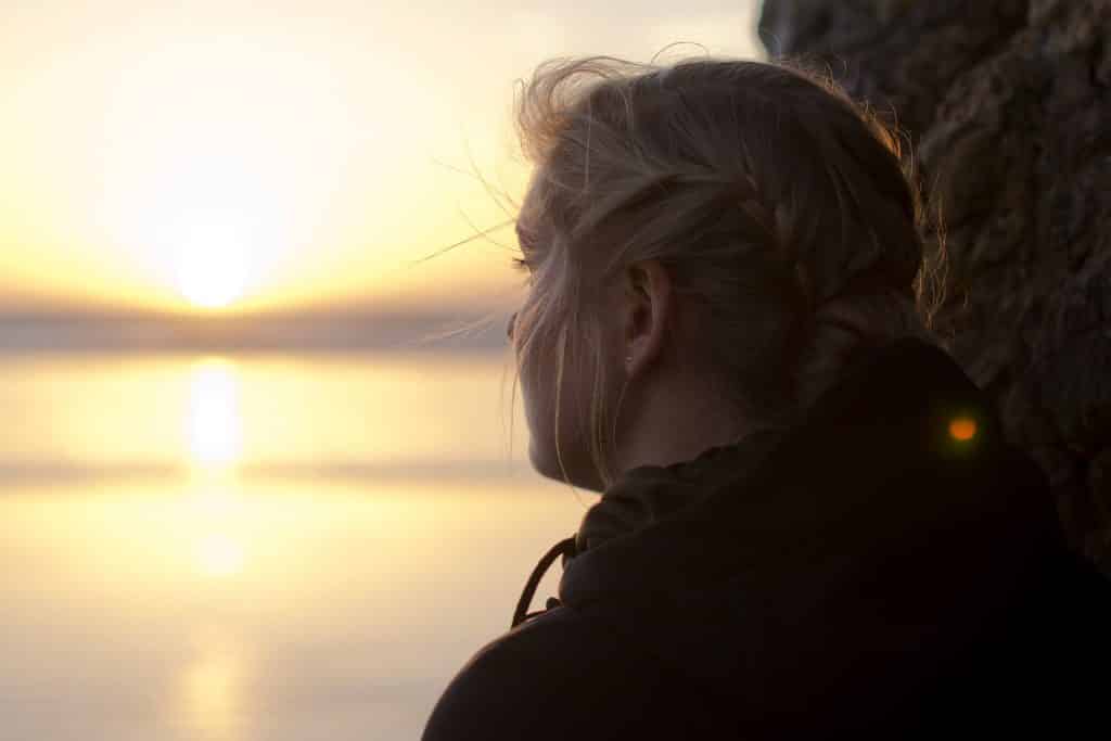 Mulher olhando para o pôr do sol em um rio.