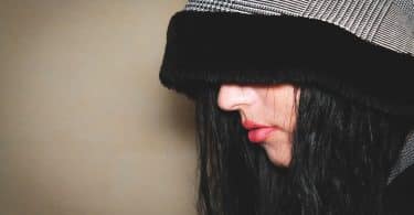 Imagem do rosto de uma mulher de lado. Ela usa uma touca cinza com barrado preto. A touca cobre toda a parte superior da cabeça e dos olhos. Ela está de mau humor.