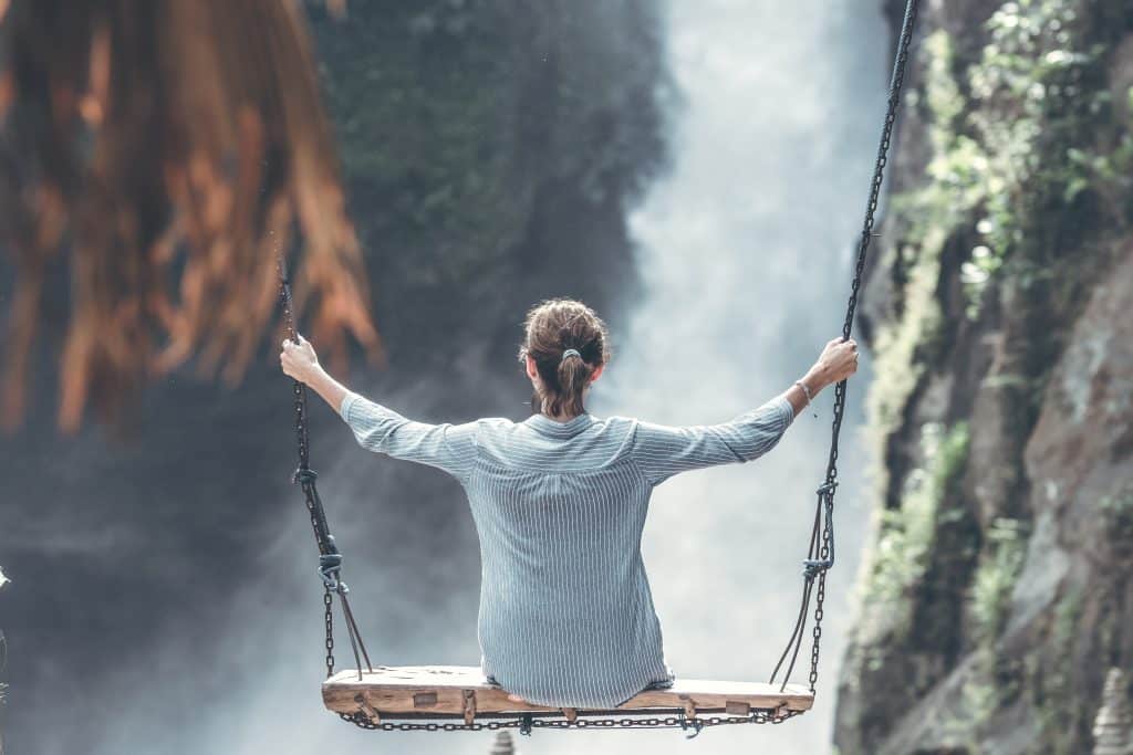 Mulher em um balaço de frente para uma cachoeira 