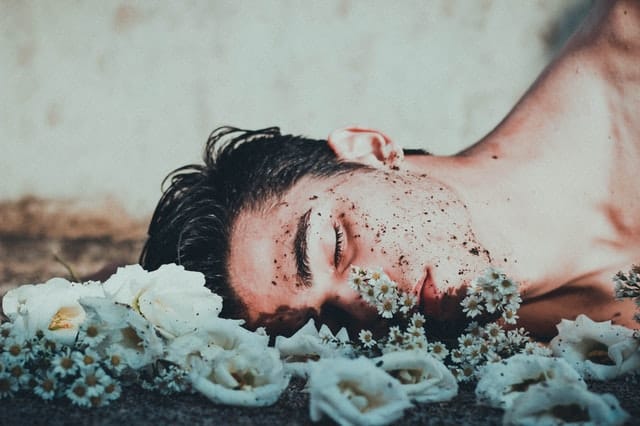 Homem com rosto no chão sujo de terra e flores em volta