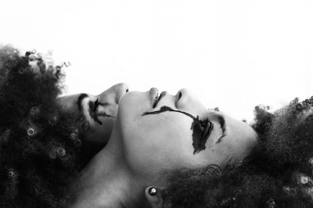 Imagem preto e branco de duas mulheres deitadas e olhando para cima com a maquiagem dos olhos escorrendo.