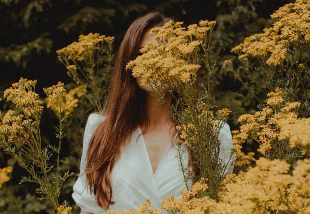 Mulher branca de cabelos atrás de ramos de flores amarelas