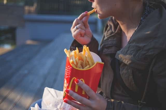 Mulher de perfil comendo batata frita