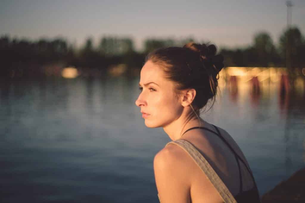 Mulher de perfil olhando para o horizonte em frente a um rio.