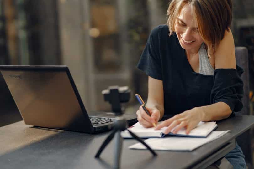 Mulher escrevendo em um caderno e sorrindo