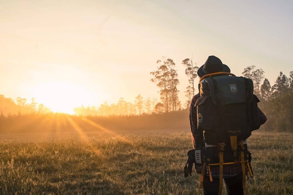 Pessoa com uma mochila grande nas costas em um campo olhando o pôr do sol.