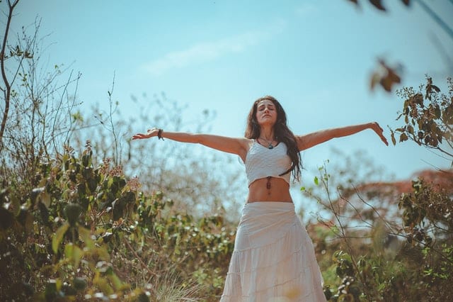 Mulher em meio a natureza com braços abertos meditando