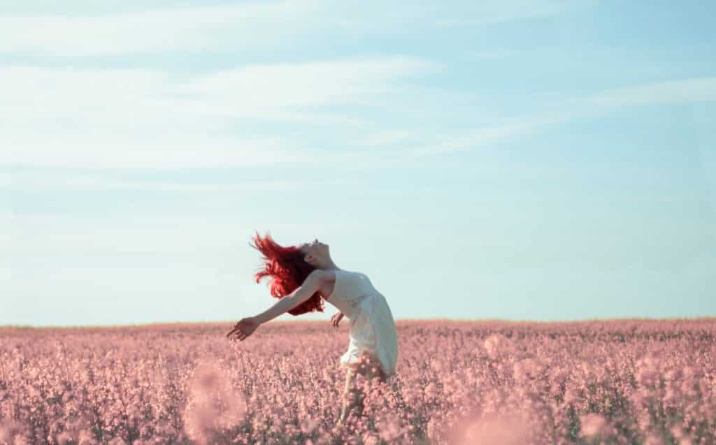 Mulher em um campo de flores com braços abertos.