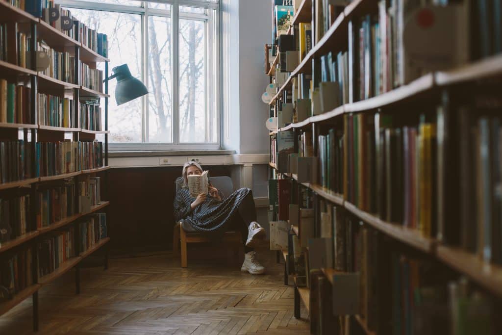 Mulher sentada em uma poltrona lendo um livro na biblioteca