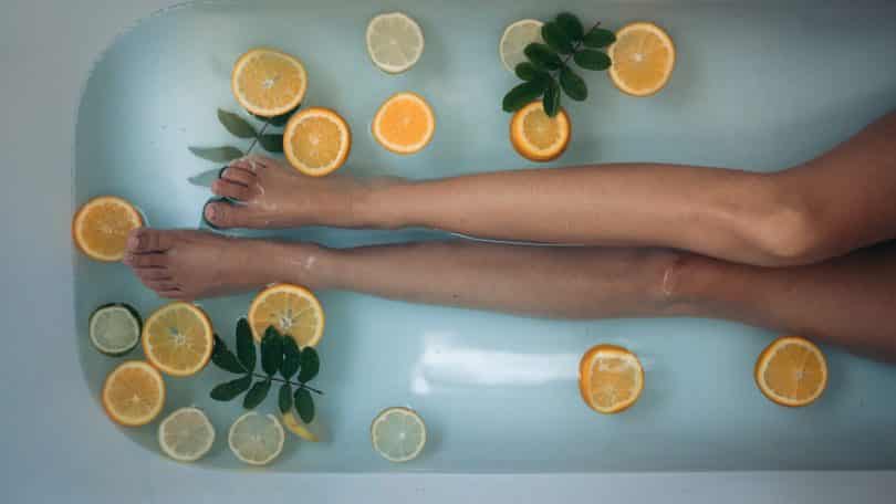Mulher deitada na banheira com folhas e laranjas em rodelas