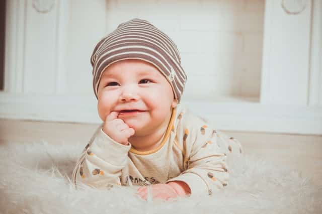 Bebê de barriga para baixo no chão sorrindo com touca na cabeça