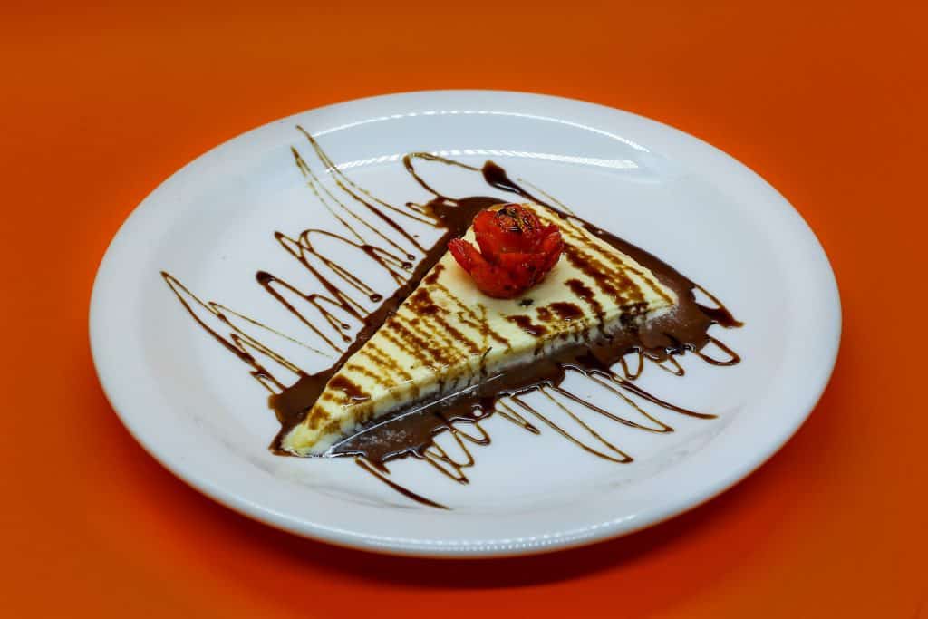 Imagem do pedaço de uma pizza doce no sabor de banana, doce de leite e chocolate. O pedaço está sendo servido e um prato de porcelana na cor branco.