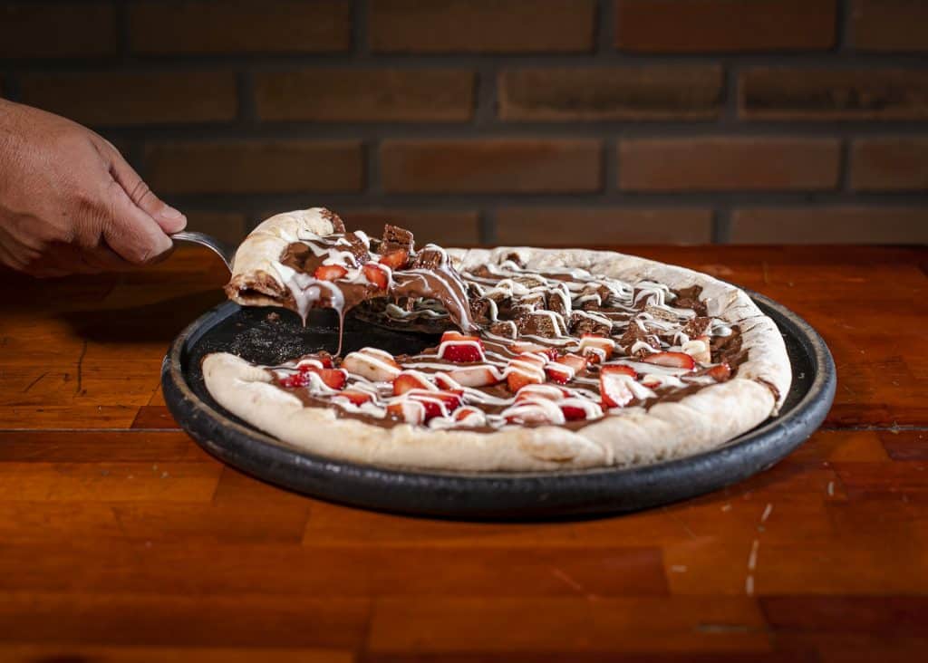 Imagem de uma pizza doce no sabeor de chocolate com morango. Ela está sendo cortada e pronta para ser servida.