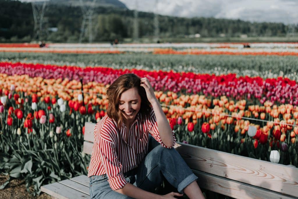 Mulher branca sentada num banco em frente a um jardim de tulipas.