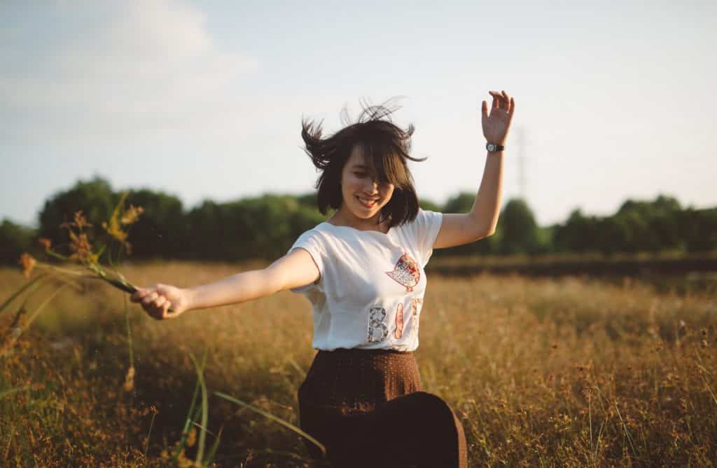 Mulher com os cabelos ao vento sorrindo em um campo de centeio.