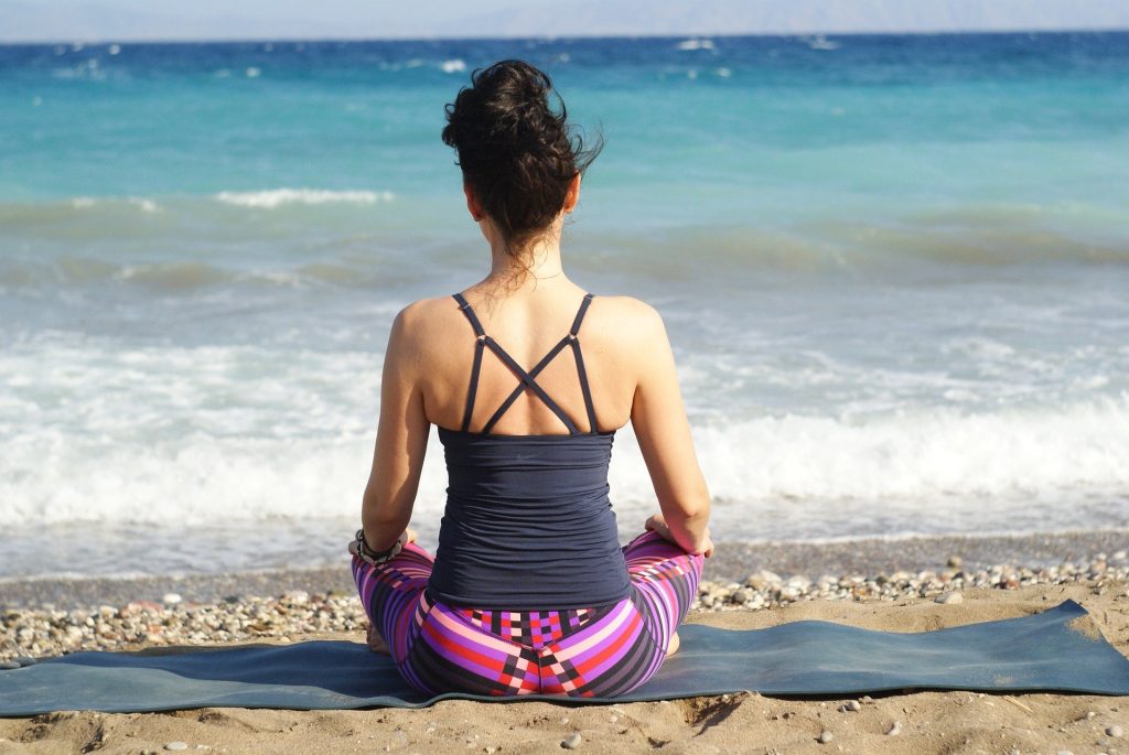 Imagem de uma mulher sentada e fazendo a sua meditação de frente para o mar.
