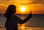 Imagem da silhueta de uma jovem fazendo uma selfie em pleno por do sol em um alto dia de verão.