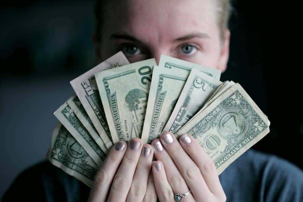 Mulher escondendo seu rosto em um leque de notas de dinheiro.