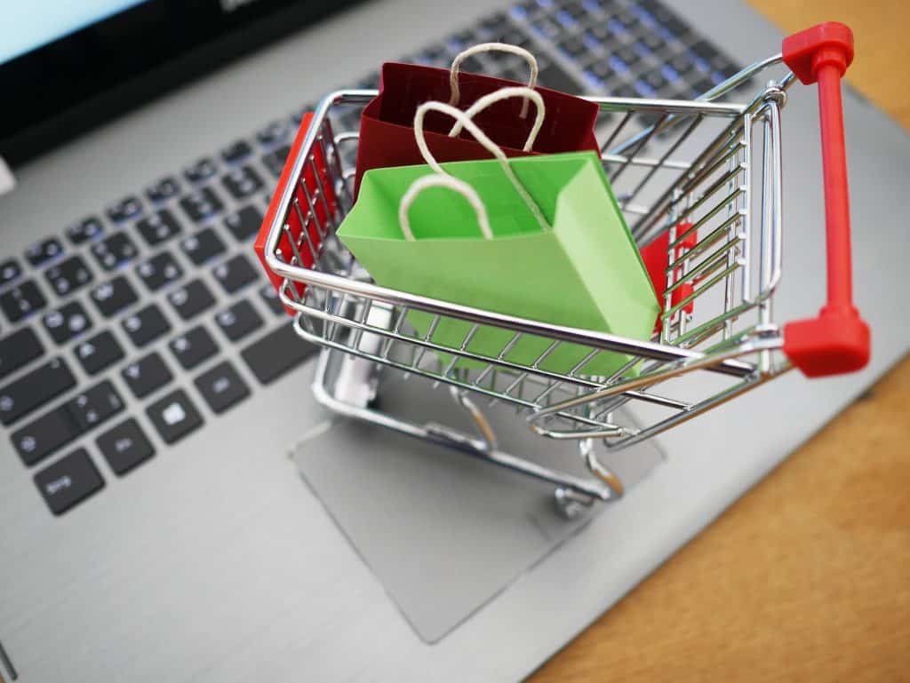 Imagem de um teclado de notebook e sobre ele uma miniatura de um carrinho de supermercado e dentro dele duas sacolas de compras vazias, sendo uma na cor verde e a outra na cor vermelha.