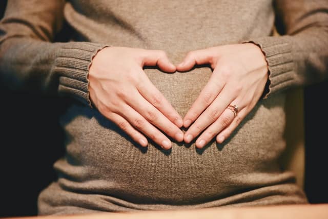 Mãos de mulher apoiada em barriga gestante formando coração