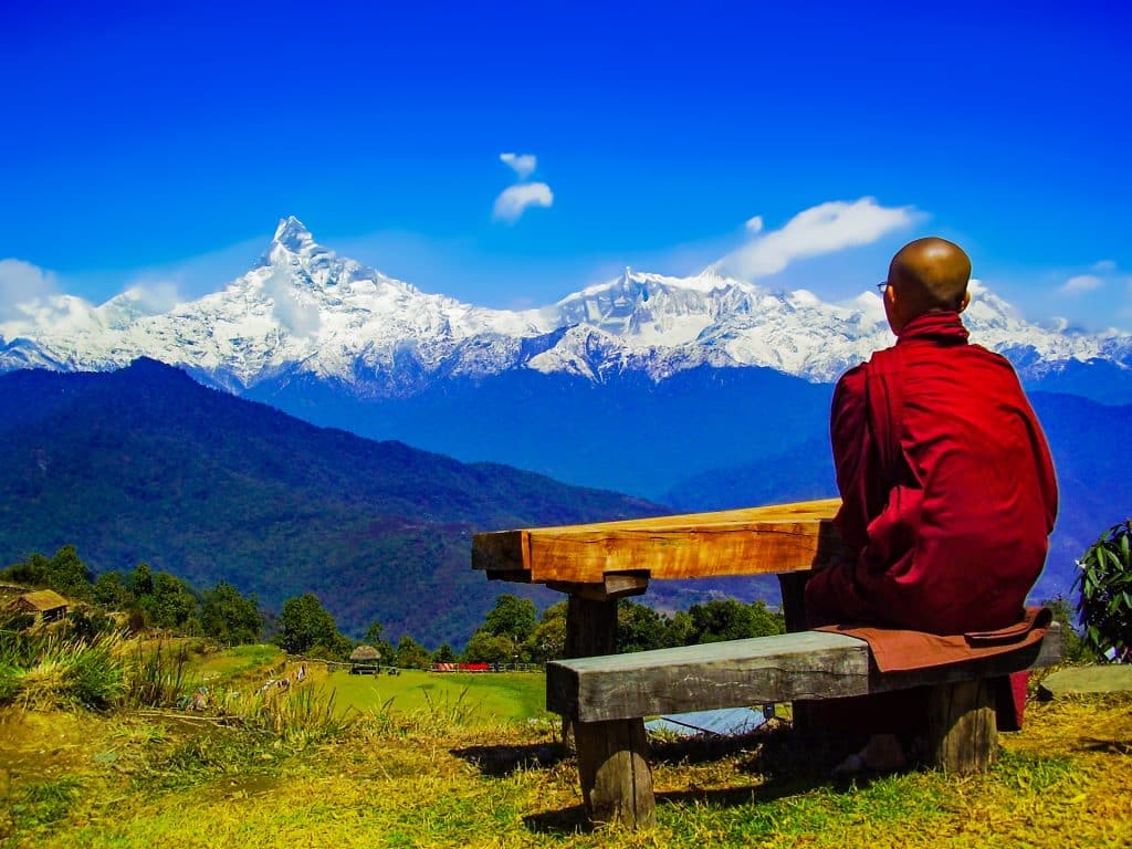 Imagem de um monge sentando em um banco feito de madeira em um retiro espiritual. Ele está em silêncio, praticando a prática.