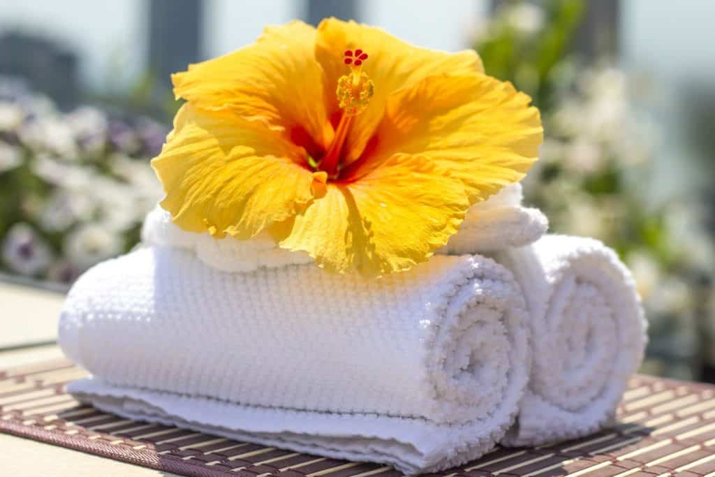 Imagem de duas toalhas brancas e de um flor de hibisco amarela sobre elas. Elas rementem as receitas de banho de assento para a candidíase.
