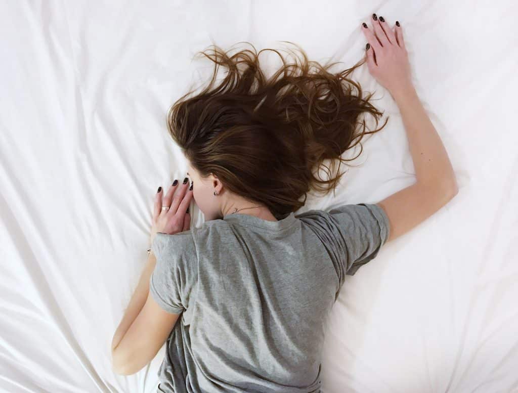 Mulher de costas deitada em uma cama com lençóis brancos.