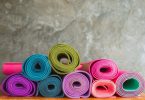 Imagem de diversos tapetes de yoga de várias cores. Eles estão enrolados dispostos sobre uma bancada.
