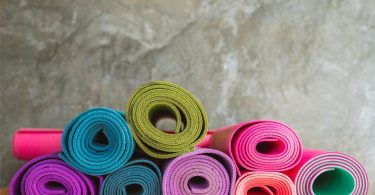 Imagem de diversos tapetes de yoga de várias cores. Eles estão enrolados dispostos sobre uma bancada.