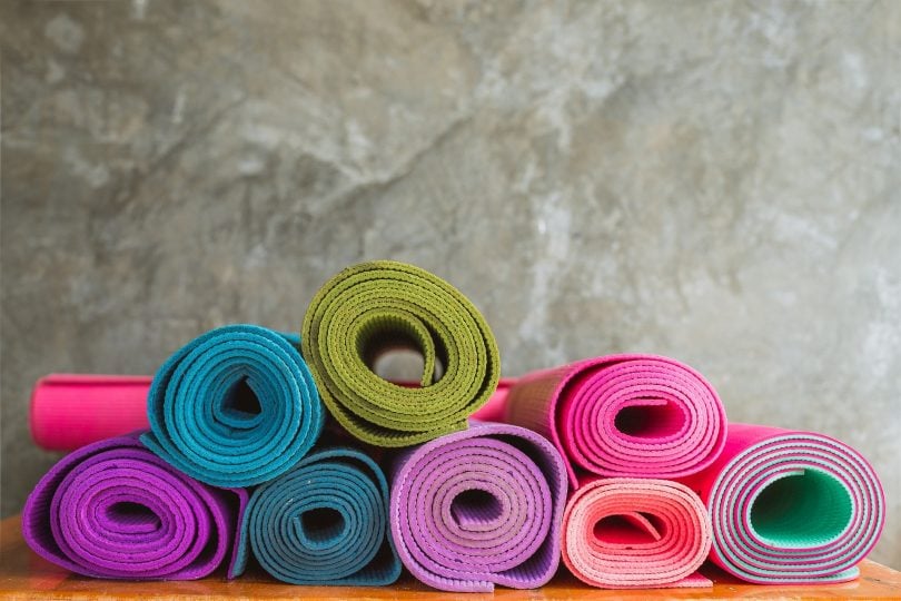 Imagem de diversos tapetes de yoga de várias cores. Eles estão enrolados dispostos sobre uma bancada.