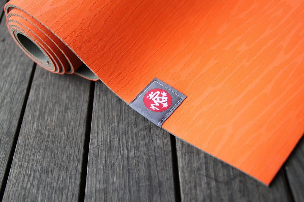 Imagem de um tapete de yoga na cor laranja disposto sobre um piso de madeira.
