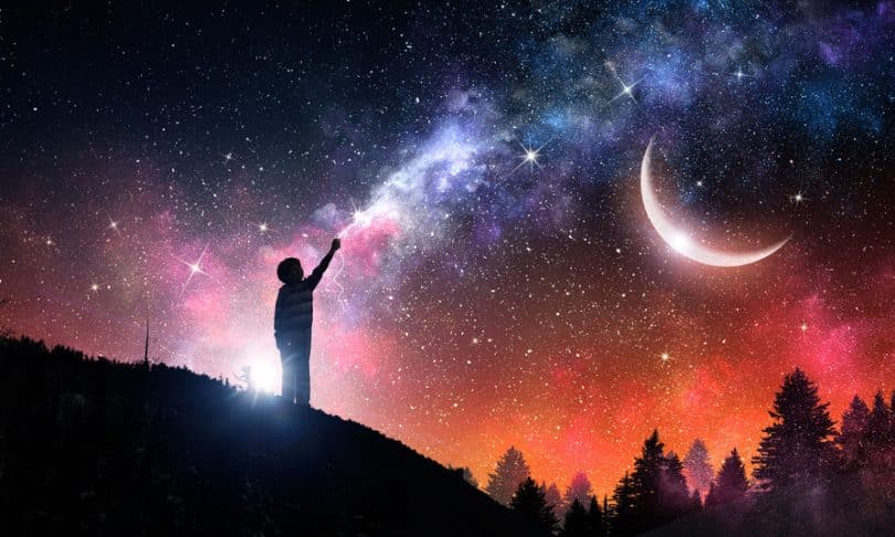 Silhueta de garoto com céu iluminado de estrelas e lua ao fundo