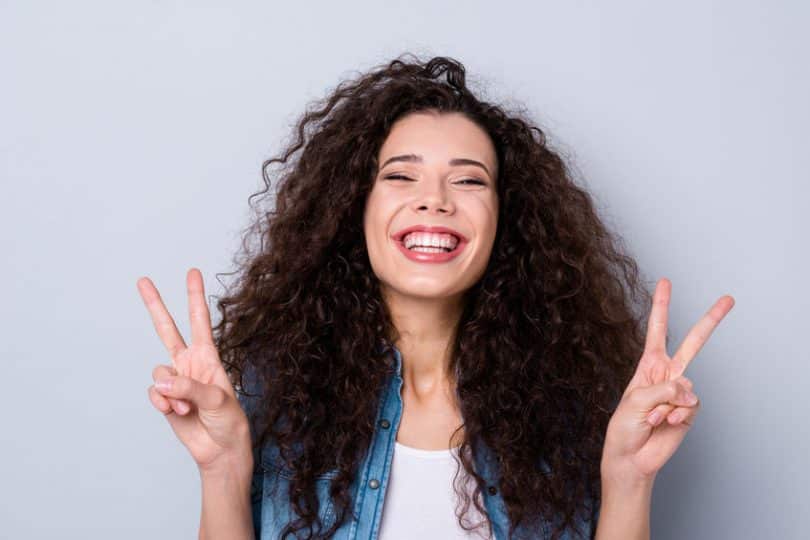 Mulher sorrindo fazendo sinal de paz e amor com as mãos