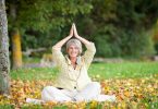 Mulher madura sentada em folhas secas meditando ded olhos fechados e sorrindo