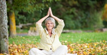 Mulher madura sentada em folhas secas meditando ded olhos fechados e sorrindo