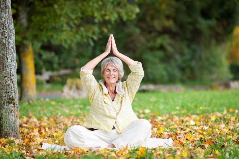 Mulher madura sentada em folhas secas meditando ded olhos fechados e sorrindo