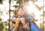 Casal abraçado sorrindo em fundo de árvores