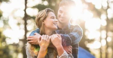 Casal abraçado sorrindo em fundo de árvores