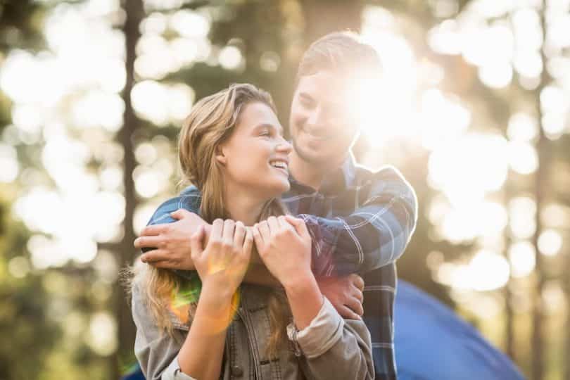 Casal abraçado sorrindo em fundo de árvores